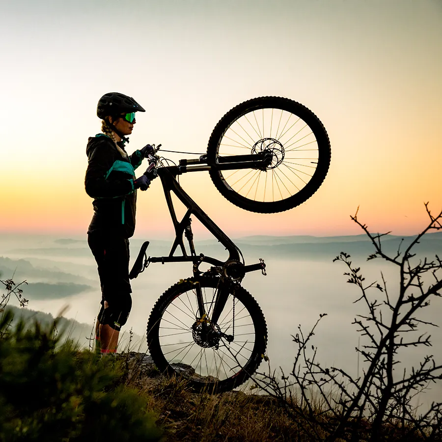 Eine Mountainbikerin steht bei Sonnenuntergang auf einem Gipfel